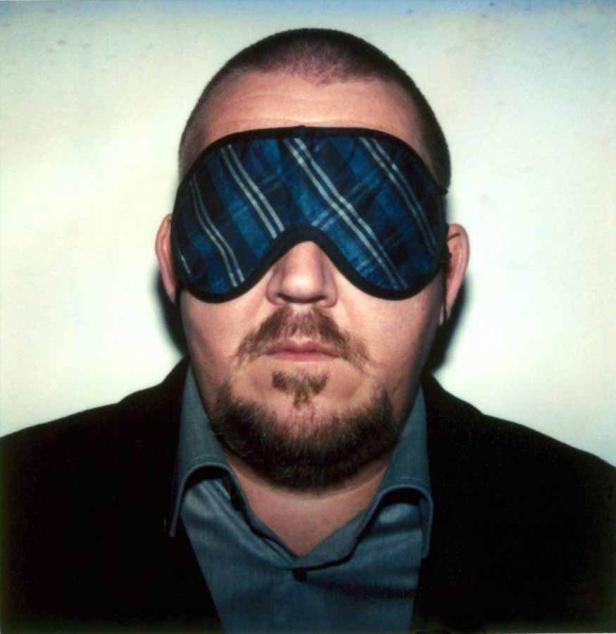 Ein Mann mit Bart und Schlafmaske vor einem hellen Hintergrund.