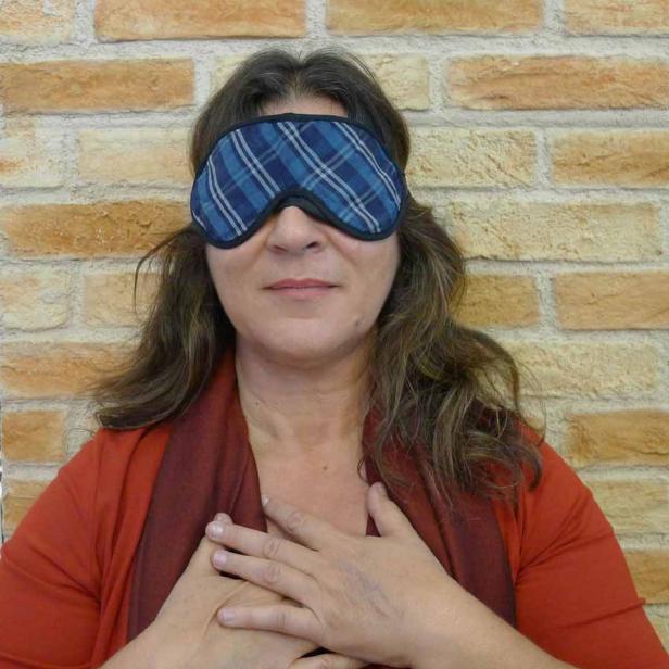 Eine Frau mit Schlafmaske legt die Hände auf ihre Brust.