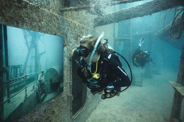 Zwei Taucher erkunden ein gesunkenes Schiffswrack unter Wasser.