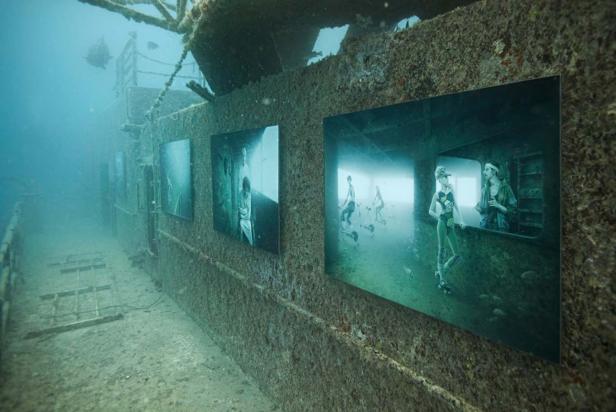 Unterwasseraufnahme eines Schiffswracks mit angebrachten Fotografien an der Wand.