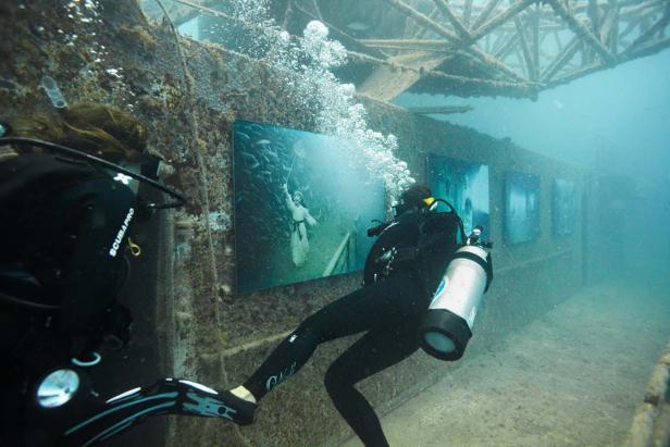 Zwei Taucher betrachten Unterwasser-Fotoausstellungen in einem versunkenen Gebäude.
