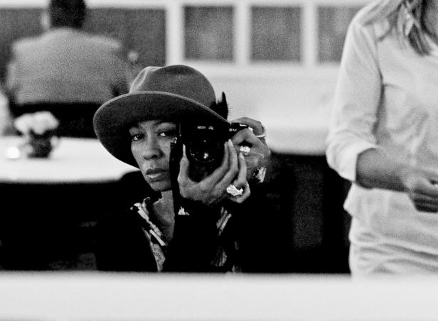 Eine Frau mit Hut fotografiert mit einer Kamera.