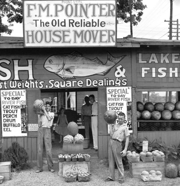 Zwei Jungen posieren mit Melonen vor einem Laden, der Fisch und Melonen verkauft.