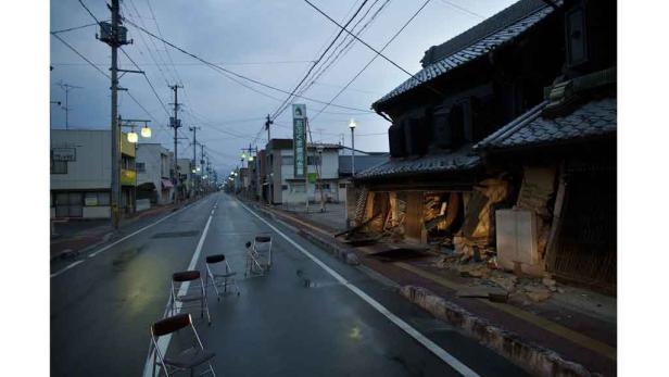 Eine verlassene Straße in Japan mit einem zerstörten Gebäude und umgestürzten Stühlen.