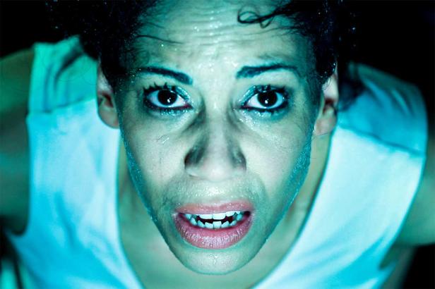 Das Gesicht einer verschwitzten Frau mit aufgerissenen Augen und leicht geöffnetem Mund.