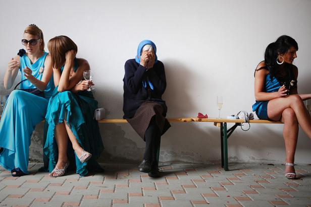 Frauen in festlicher Kleidung sitzen auf einer Bank, eine ältere Frau weint.