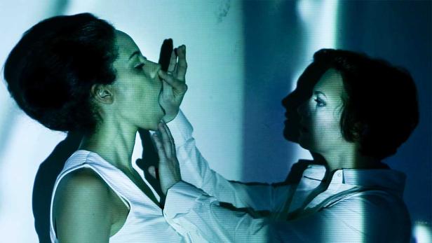 Eine Frau berührt das Gesicht einer anderen Frau vor einem blauen Hintergrund.