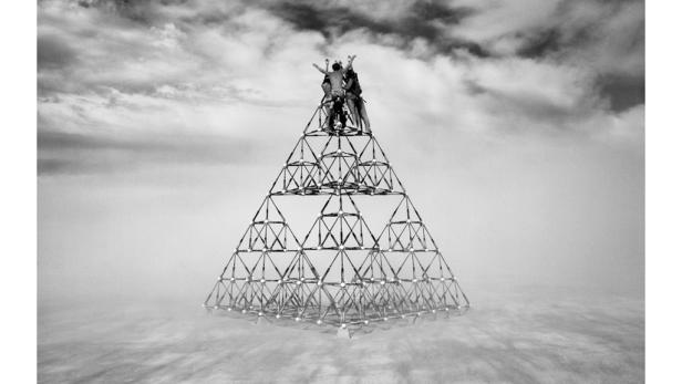 Eine Gruppe von Menschen steht auf einer pyramidenförmigen Struktur unter einem bewölkten Himmel.