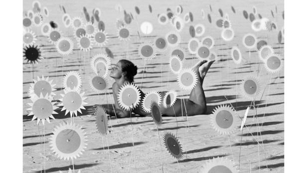 Eine Frau liegt inmitten von stilisierten Sonnenblumen am Strand.