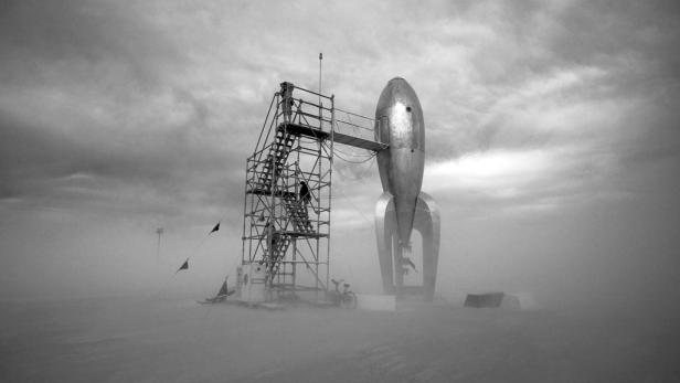 Eine silberne Rakete steht neben einem Gerüst in einer nebligen Landschaft.