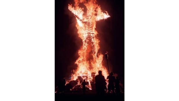 Eine große Holzkonstruktion in Form einer menschlichen Figur steht in Flammen, umgeben von Menschen.