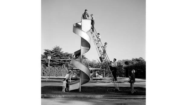 Eine Gruppe von Menschen, darunter Kinder, nutzen eine spiralförmige Rutsche auf einem Spielplatz.