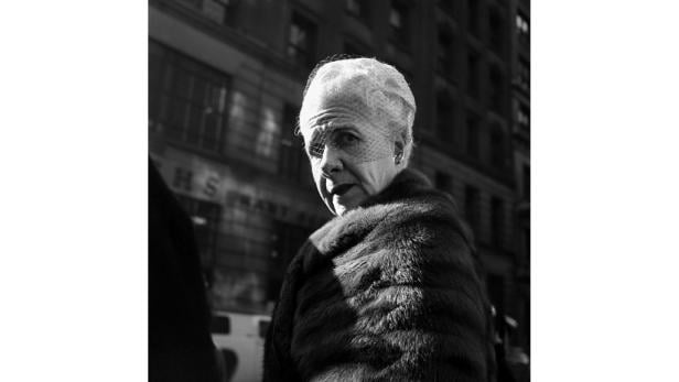 Eine ältere Dame mit Hut und Pelzmantel blickt in die Kamera.