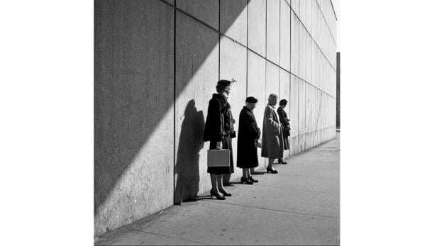Eine Gruppe elegant gekleideter Frauen wartet vor einer Wand im Schatten.