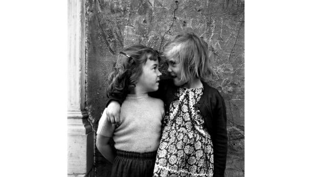 Zwei kleine Mädchen stehen eng beieinander und schauen sich an.