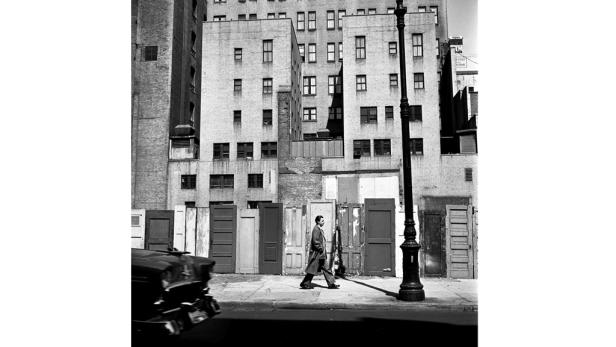 Ein Mann geht auf dem Bürgersteig an einer Reihe von Türen vorbei.