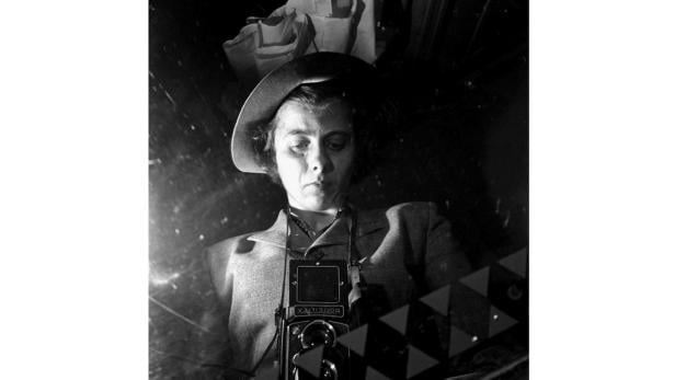 Eine Frau mit Hut und Jackett fotografiert mit einer Rollei-Kamera.