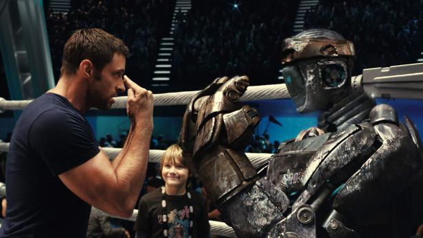 Hugh Jackman und ein Kind stehen einem Kampfroboter in „Real Steel“ gegenüber.