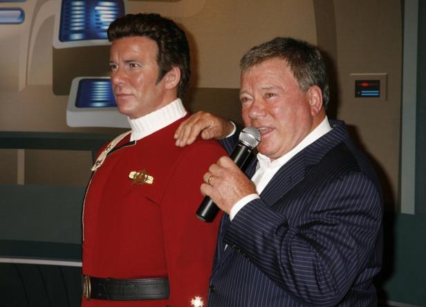 William Shatner mit Mikrofon neben einer Wachsfigur von Captain Kirk.