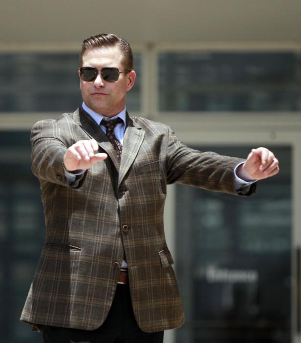 Ein Mann mit Sonnenbrille und kariertem Sakko gestikuliert.