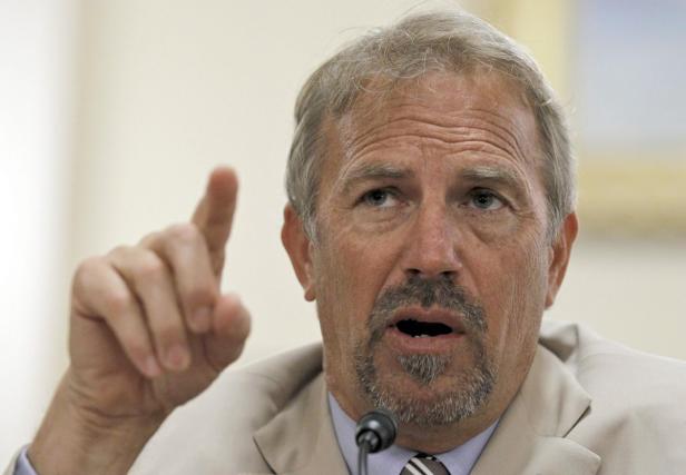 Kevin Costner gestikuliert während einer Rede vor einem Mikrofon.