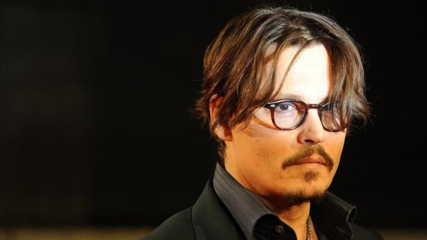 Porträt von Johnny Depp mit Brille und Bart vor einem dunklen Hintergrund.