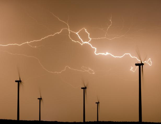 Blitze zucken über Windrädern am Himmel.