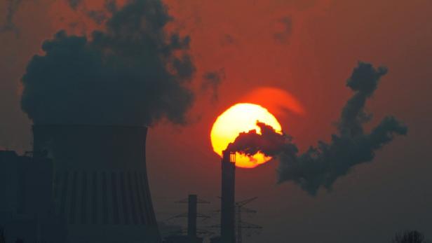 Ein Kohlekraftwerk bei Sonnenuntergang stößt Rauch aus.