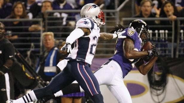 Ein Footballspieler der Ravens fängt den Ball, während ein Spieler der Patriots ihn zu stoppen versucht.