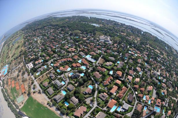 Luftaufnahme einer Wohngegend mit vielen Häusern, Pools und Grünflächen in Küstennähe.