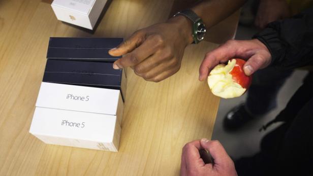 Mehrere iPhone 5-Verpackungen und eine angebissene Apfel auf einem Tisch.