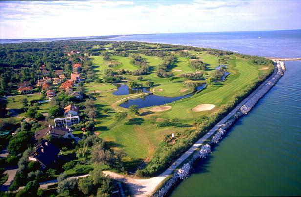 Luftaufnahme eines Golfplatzes an der Küste mit Wohnhäusern im Hintergrund.
