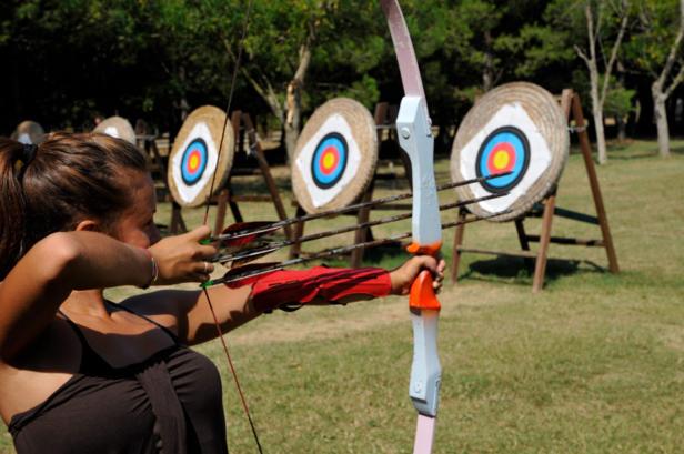 Eine Frau zielt mit Pfeil und Bogen auf Zielscheiben im Freien.