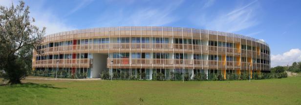 Ein modernes, rundes Gebäude mit Holzverkleidung und großen Fenstern unter blauem Himmel.