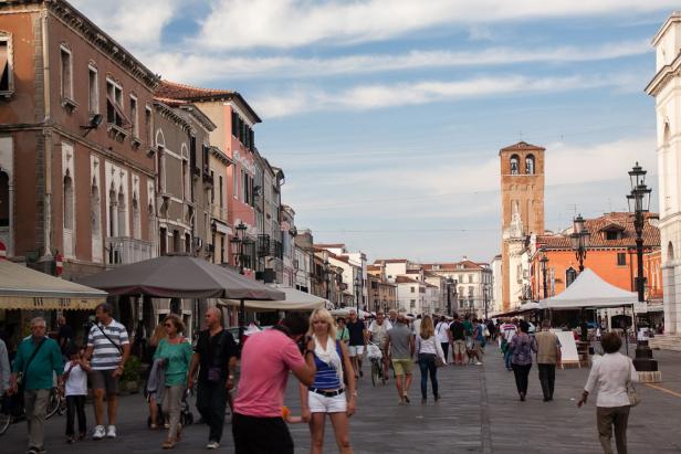 Eine belebte Straße in Venedig mit Menschen und einem Glockenturm im Hintergrund.