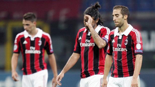 Drei Fußballspieler des AC Mailand in rot-schwarzen Trikots wirken enttäuscht.