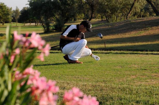 Ein Golfspieler hockt auf dem Grün und platziert einen Golfball.