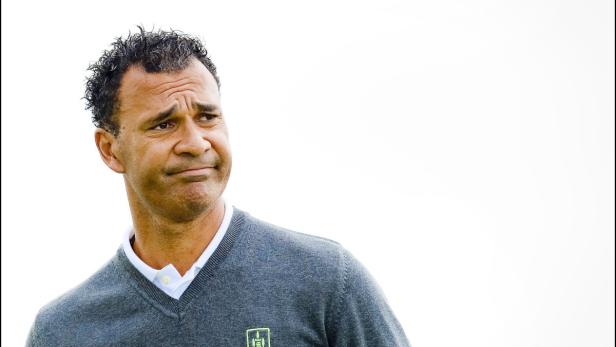 Ein Mann mit dunklen Haaren und einem grauen Pullover blickt nachdenklich zur Seite.