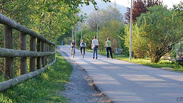 Zwei Personen fahren mit dem Fahrrad, eine Person geht Inlineskaten auf einem Weg.