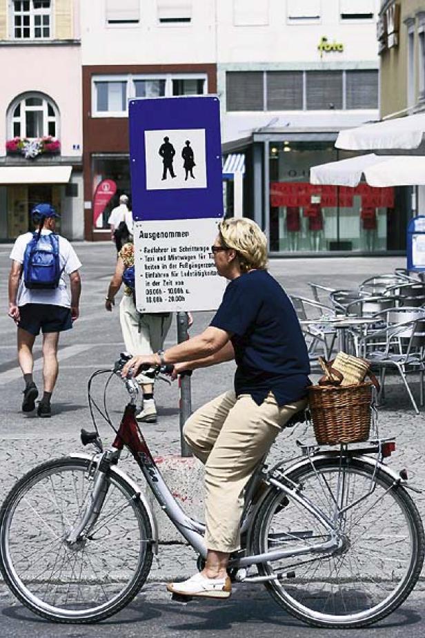 Eine Frau fährt mit dem Fahrrad durch eine Fußgängerzone.
