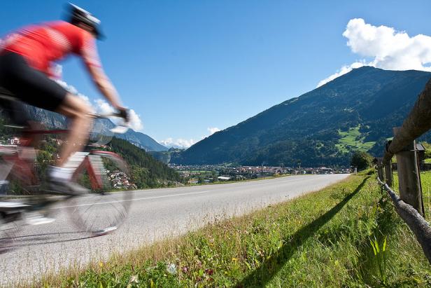 Ein Radfahrer fährt auf einer Landstraße vor einer Bergkulisse.