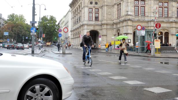 Ein Mann fährt mit einem blauen Fahrrad auf einer nassen Straße in Wien.