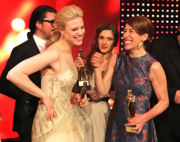 Mehrere Frauen mit goldenen Statuen lächeln auf einer Preisverleihung.