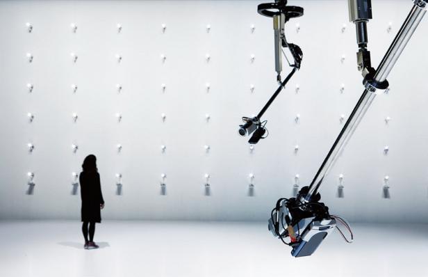 Eine Frau steht vor einer Wand mit leuchtenden Objekten, die von Roboterarmen gehalten werden.