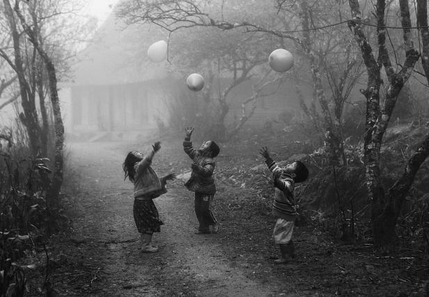 Drei Kinder spielen im Nebel mit Ballons.