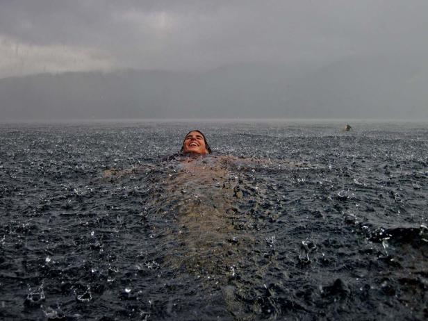 Eine Frau schwimmt lachend im Regen in einem See.