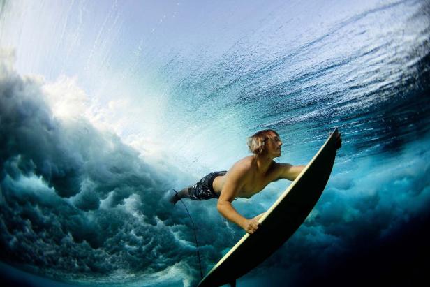 Ein Surfer taucht mit seinem Surfbrett unter einer Welle hindurch.