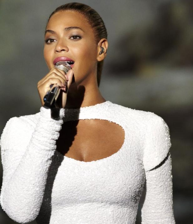 Beyoncé singt in einem weißen Kleid mit einem Mikrofon in der Hand.