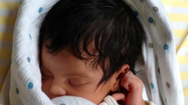 Ein neugeborenes Baby schläft, in eine Decke mit blauen Punkten gewickelt.