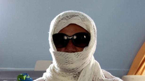 Eine Person mit Sonnenbrille und einem weißen Tuch um den Kopf.